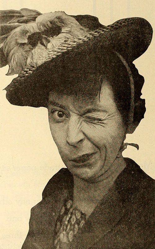 Photographie en couleur sépia d'une femme portant un chapeau à large bord orné d'une plume et faisant un clin d'œil d'une manière exagérée.