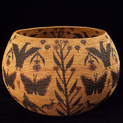 A color photograph of a low, round handwoven basket, which narrows at the top to form an opening. The background shade of the basket is light tan. Images of flowers, birds, and butterflies are woven into the basket using materials of darker tones.