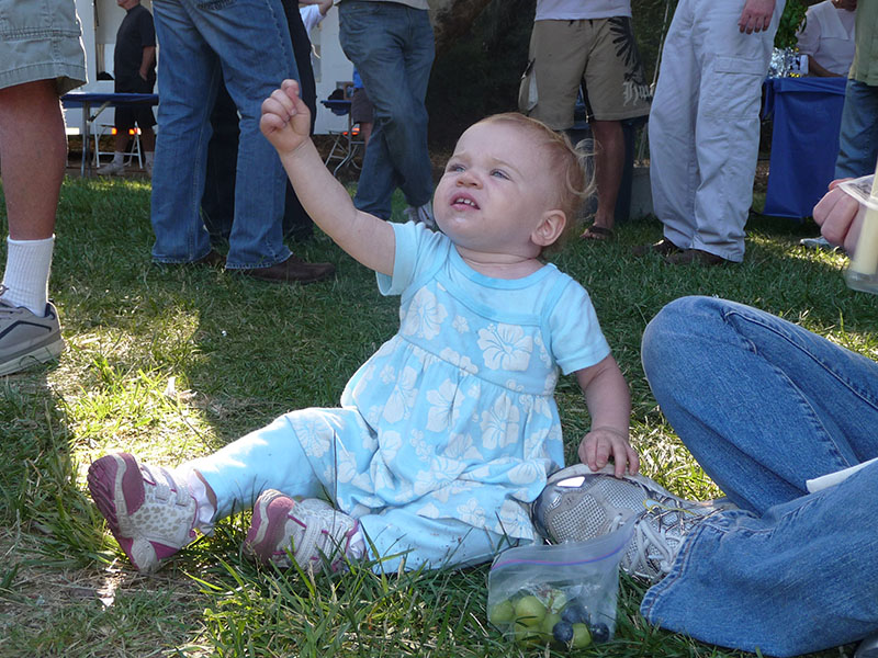 一个小孩坐在草地上。 她举起右手悬在空中，拇指藏在剩下的手指下方。