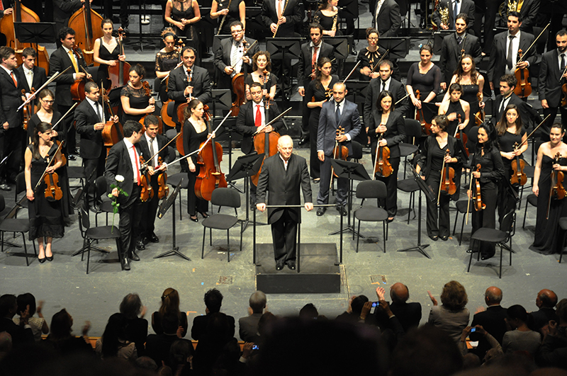 Membros da orquestra estão em pé para agradecer aplausos no final de uma apresentação.
