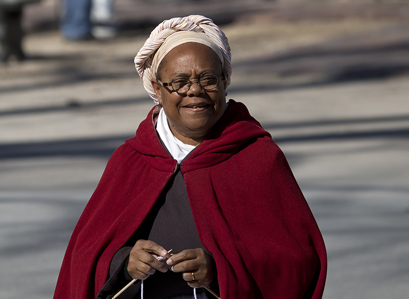 在 Clonial Williamsburg 身着传统服装的女人她戴着头巾和斗篷。 她拿着编织针。