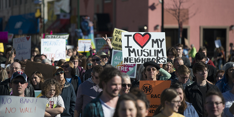 一群人挤满城市街道的彩色照片。 许多人带有标志。 照片中央突出的是手写的大标语，上面写着 “我爱我的穆斯林邻居”。 还可以看到一只举起的手展示和平标志。
