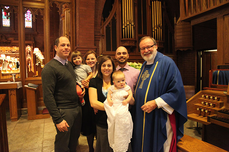 一个家庭在教堂里，有一个牧师和两个孩子，一个穿着洗礼服，还有他们的父母和宝宝的教父。