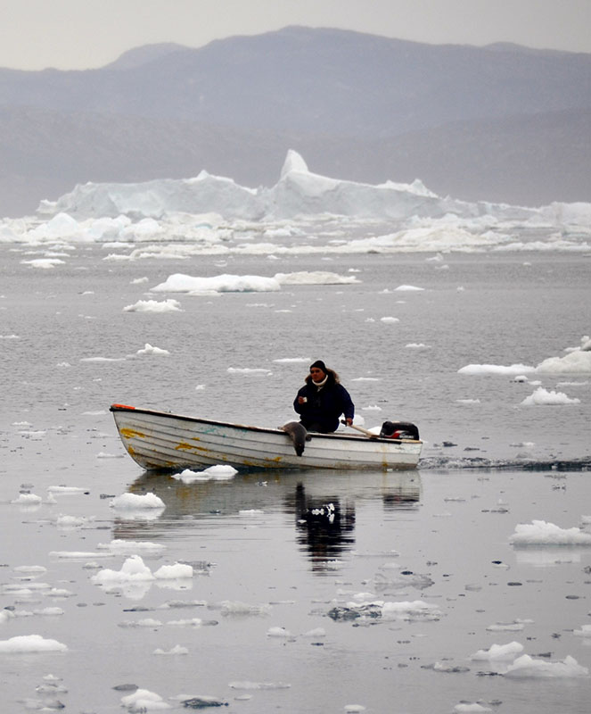 A lone man steers a small motorboat through ice-strewn water.