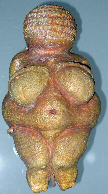 Pequena estatueta de pedra com corpo de mulher. A estatueta tem seios grandes e barriga redonda.