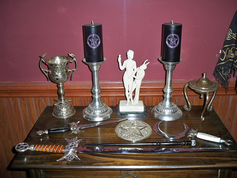 一张小木桌，上面摆放着各种物体。 这些物品包括两个人物的雕像、两个带有银色底座的高大烛台、一把刀和一把带有精致刀柄的剑以及一个银圣杯。