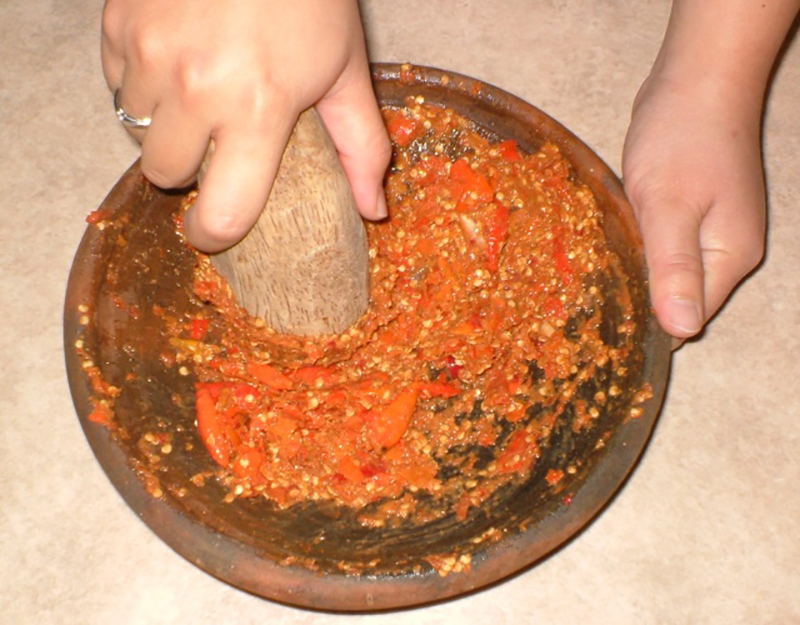 一个人用研浆和杵研磨辣椒的特写照片，只有双手可见。