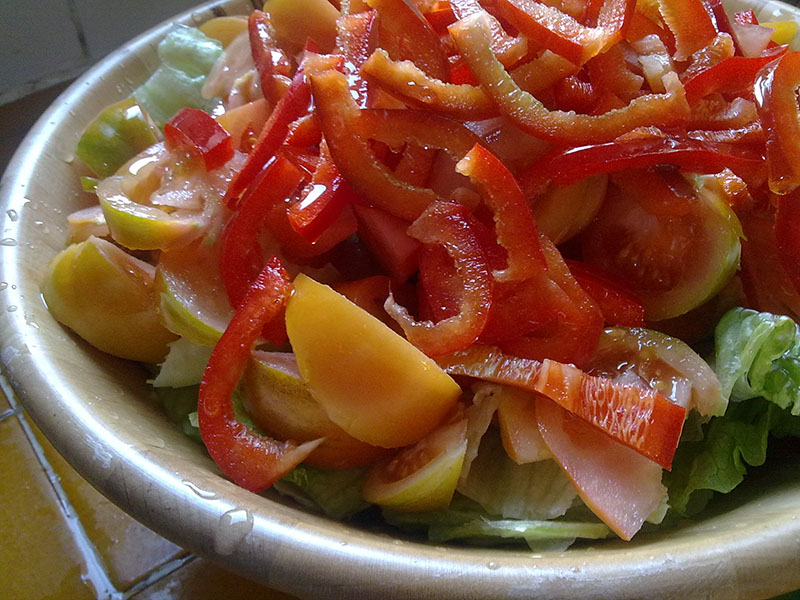 A large bowl filled with sliced red peppers, yellow tomatoes, cucumbers, and lettuce.