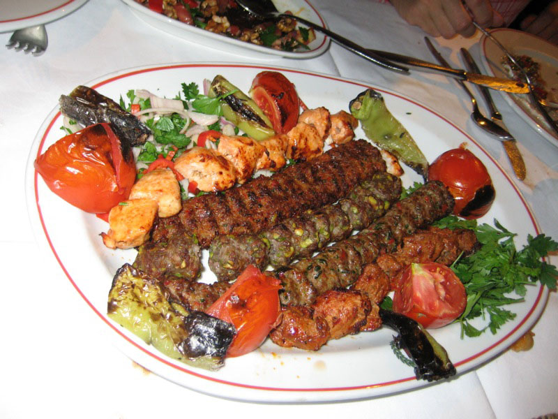 一盘鸡肉和牛肉烤肉串，周围环绕着烤番茄和辣椒。