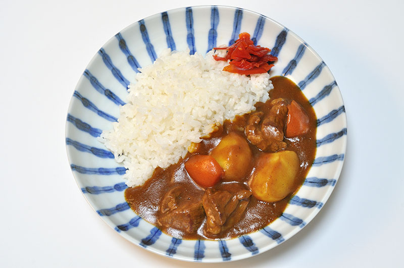 Assiette contenant du riz blanc sur une moitié et un ragoût avec des morceaux de bœuf, des pommes de terre et des carottes sur l'autre moitié.