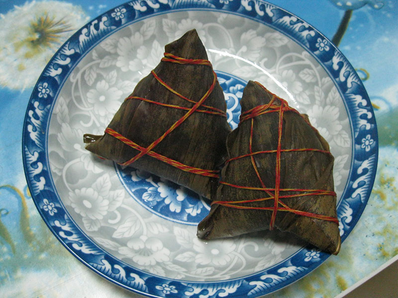 Two triangular-shaped packets of food on a plate, wrapped in bamboo leaves and tied with string.