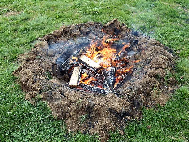 Des bûches et des cendres fumantes dans un brasero dans un champ.
