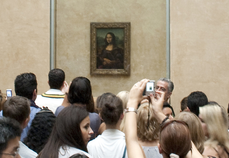 一群参观博物馆的人正在观看《蒙娜丽莎》。 一个人用手机拍照。