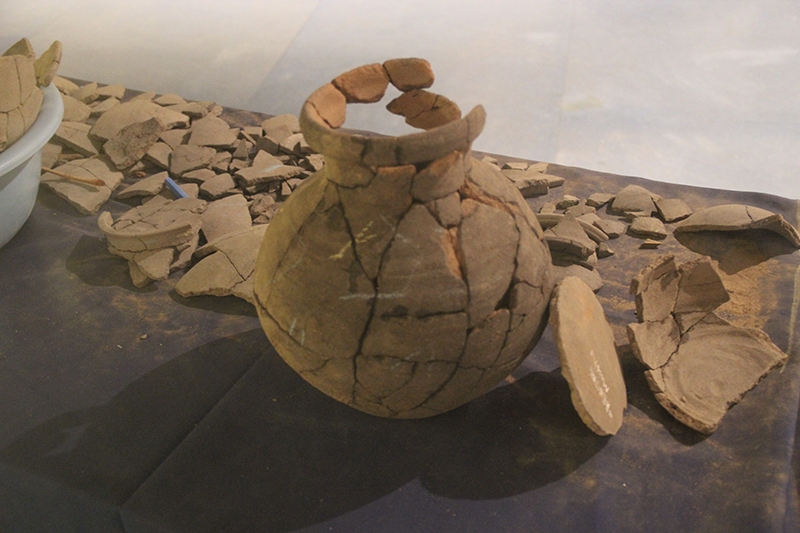 Estilhaços de cerâmica - alguns dispostos sobre uma mesa e outros encaixados para formar a maior parte de um vaso.