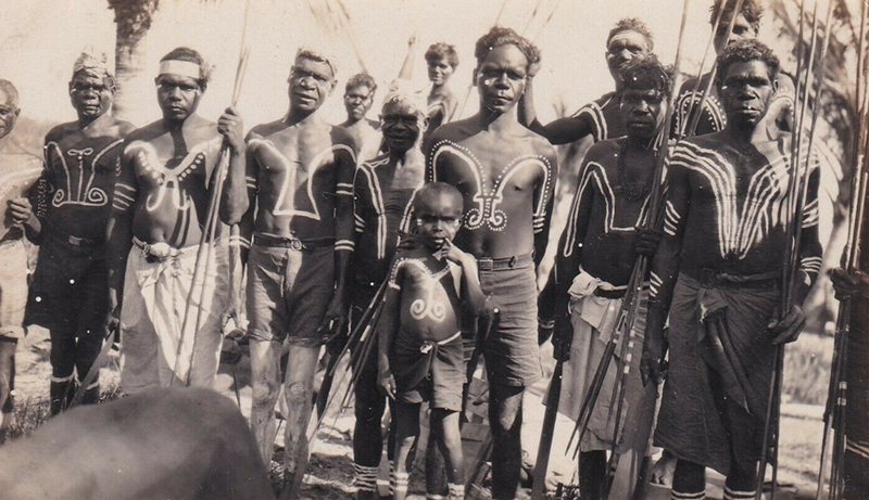 Black and white photograph of a group of people with geometric designs painted on their torsos. The group includes grown men and boys.
