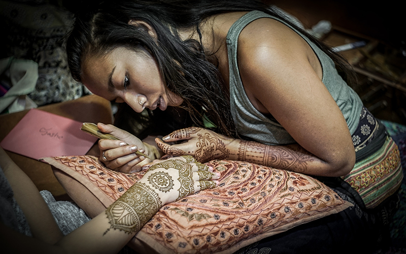 Une femme aux mains et aux avant-bras peinte au henné peignant les mains et les avant-bras d'une autre femme.
