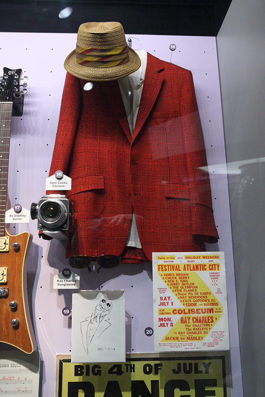 Suit jacket, hat, and guitar in a glass display case.