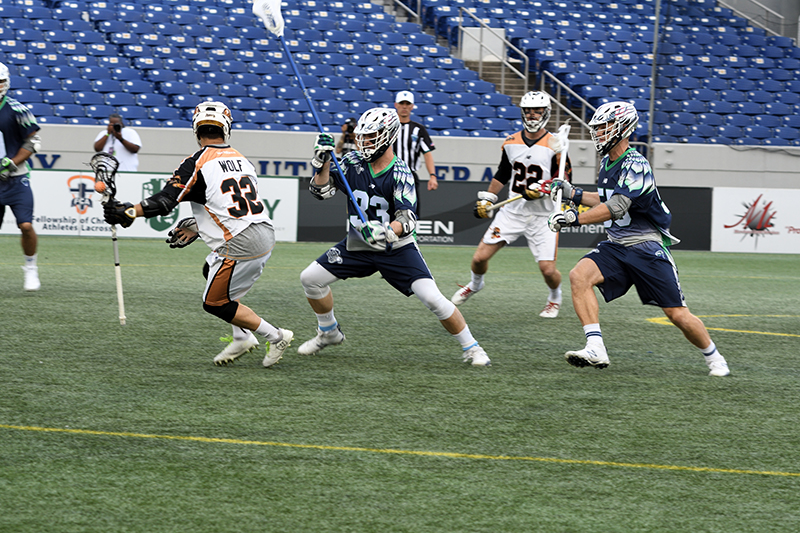 Jogadores de lacrosse vestindo uniformes e capacetes profissionais no meio de um jogo.