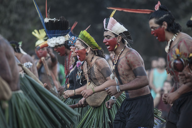 تؤدي مجموعة من الأشخاص الذين يرتدون أغطية الرأس الملونة المصنوعة من الريش وطلاء الجسم رقصة جماعية.