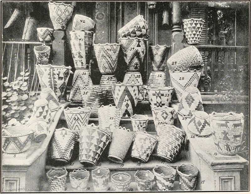 Coleção de aproximadamente 40 cestos dispostos nos degraus e corrimões de uma varanda. Eles exibem uma variedade de formas, padrões e técnicas de construção.