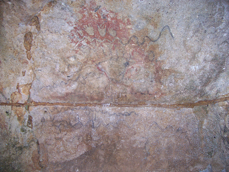 Cave wall with images of bear paws. Red paint has been applied behind the paws, making them more visible.