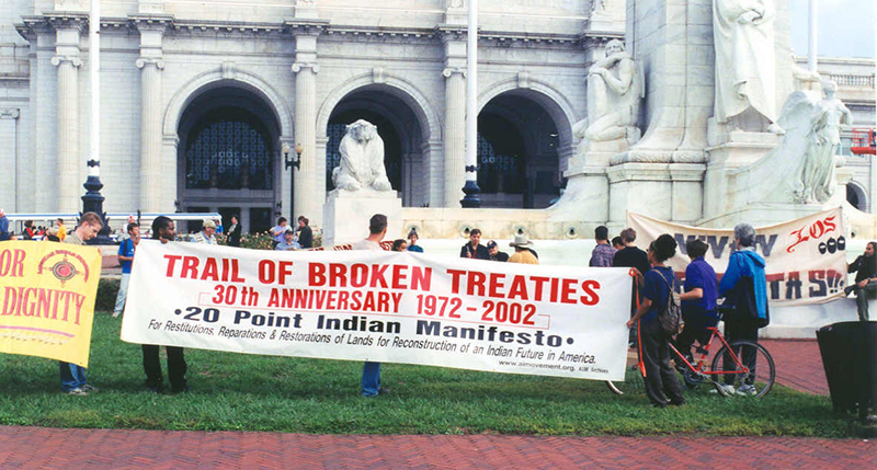 احتجاج أمام مبنى ذو مظهر رسمي بأعمدة حجرية بيضاء وأسد من الحجر الأبيض. يظهر في الصورة لافتة مكتوب عليها «درب الدموع المكسورة - الذكرى الثلاثين 1971-2002 - البيان الهندي المكون من 20 نقطة»