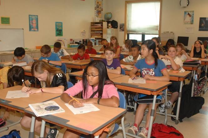 Un aula primaria de niños con diferentes colores de piel sentados en escritorios.