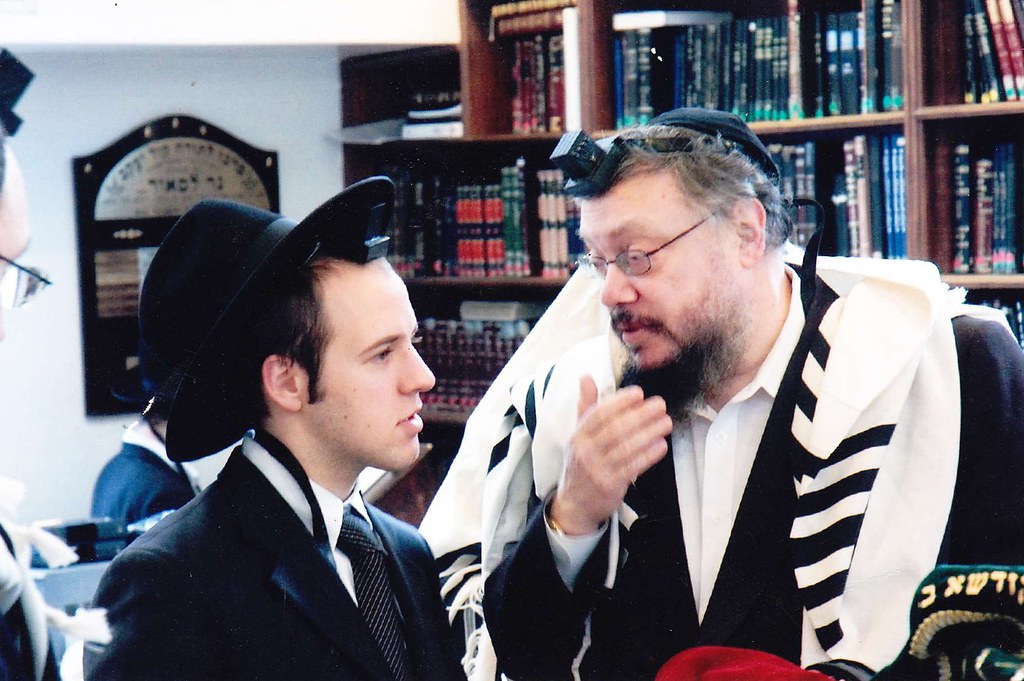Un judío jasídico mayor hablando con un hombre más joven con sombrero.