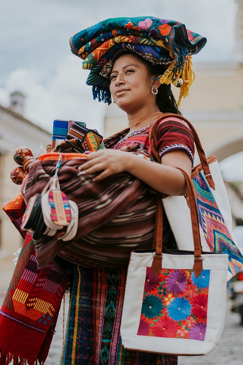 Una mujer sosteniendo telas coloridas y bolsas, sonriendo.