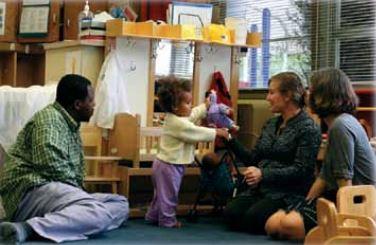 A toddler showing two caregivers a toy.