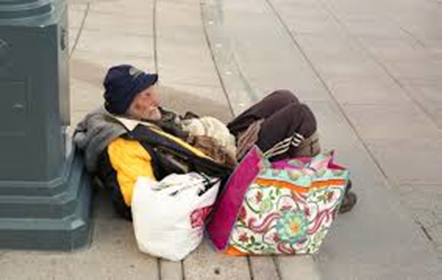 Homeless man with white beard lying on the sidewalk with two bags of belongings