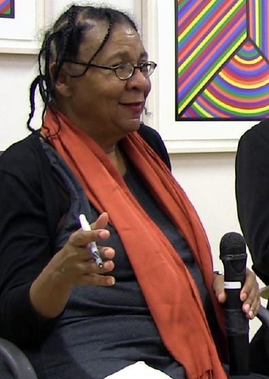 A photo of bell hooks wearing an orange scarf with a mic in her hand