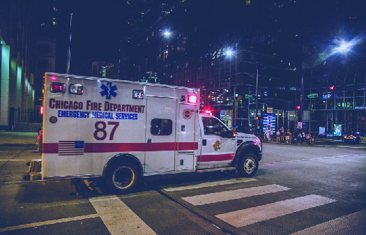 一辆带闪光灯的卡车驶过十字路口的图像。 卡车侧面写着 “芝加哥消防局紧急医疗服务”。