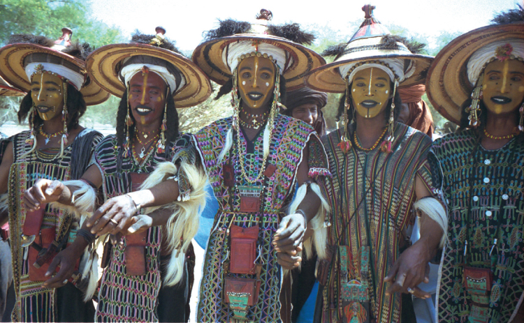 Figura 1.4. Los hombres wodaabe (de la región del Sahel de África) visten maquillaje y bailan con vestimenta elaborada para una competencia anual de rituales de cortejo. Las mujeres seleccionan al hombre más atractivo para casarse. Dan Lundberg; CC BY-SA 2.0.