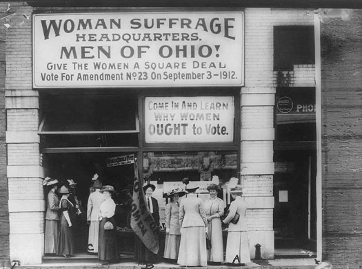 这张照片显示了妇女选举权总部外的几名妇女。 一个大标语写着 “妇女选举权总部”。 俄亥俄州的男人！ 给女人一笔平价优惠。 1912 年 9 月 3 日投票支持第 23 号修正案。” 第二个标语写着：“进来看看为什么女性应该投票。”