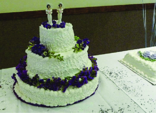 Uma foto de um bolo com três camadas. Duas estatuetas humanas aparecem na camada superior.