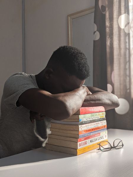 Un hombre está durmiendo con la cabeza agachada sobre una pila de libros.