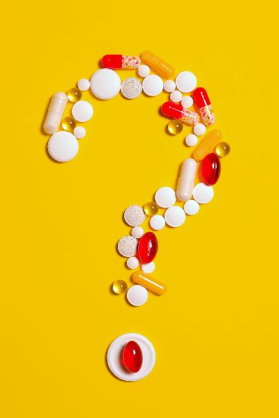 Medication pills are arranged in the shape of a question mark on a yellow background.