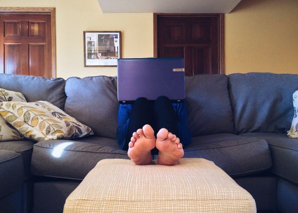 Una persona está usando una computadora portátil mientras está sentada en un sofá con las piernas apoyadas.