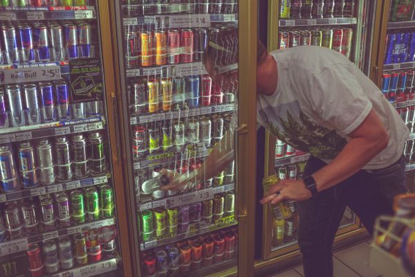 Un hombre está metiendo la mano en un enfriador de bebidas en una tienda de conveniencia y sacando una copa.