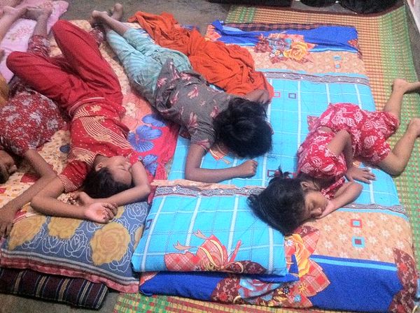 Young kids sleeping together on a pallet of blankets on the floor.
