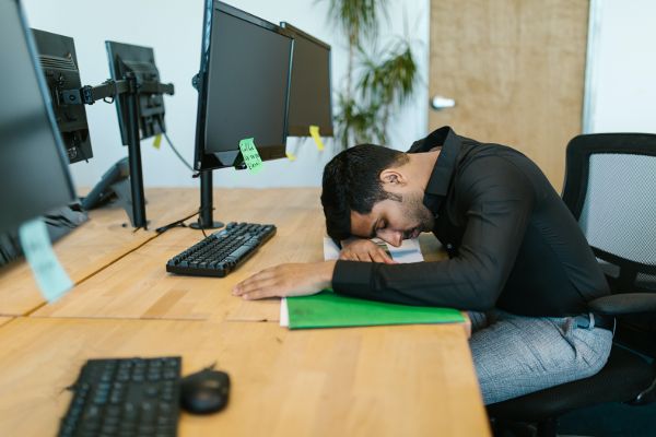 Hombre con camisa larga de manga negra dormido frente a su computadora.