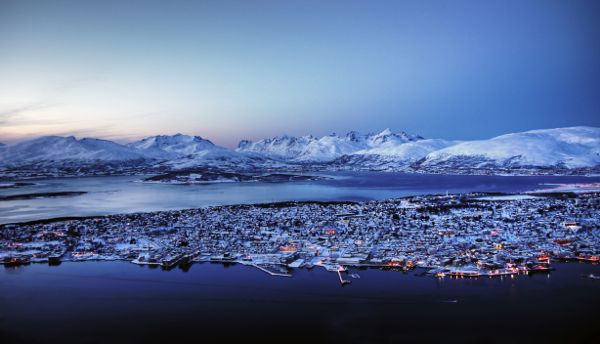An illuminated night in Tromso, a snow covered town surrounded by ocean and small mountains.