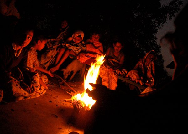 Kids surround a glowing red fire at night.