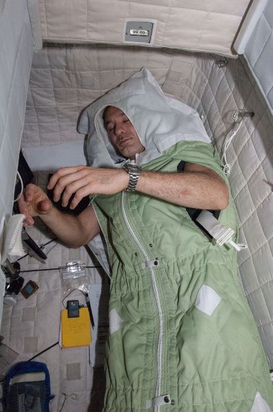 An astronaut is sleeping in a self containing sleeping bag in space.
