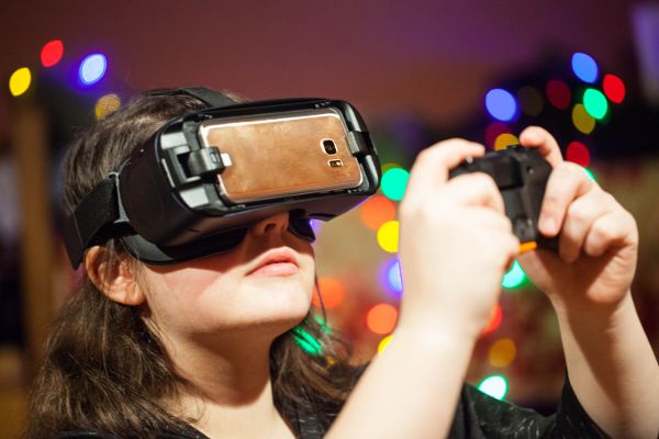 A girl wearing virtual reality goggles and using a hand held control.
