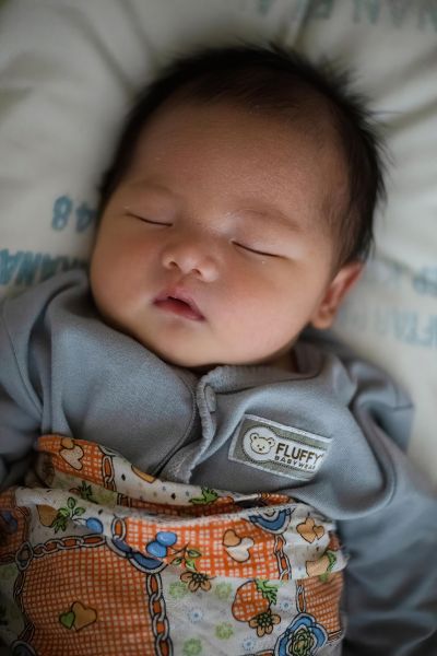 A baby in a gray onesie sleeping in bed.