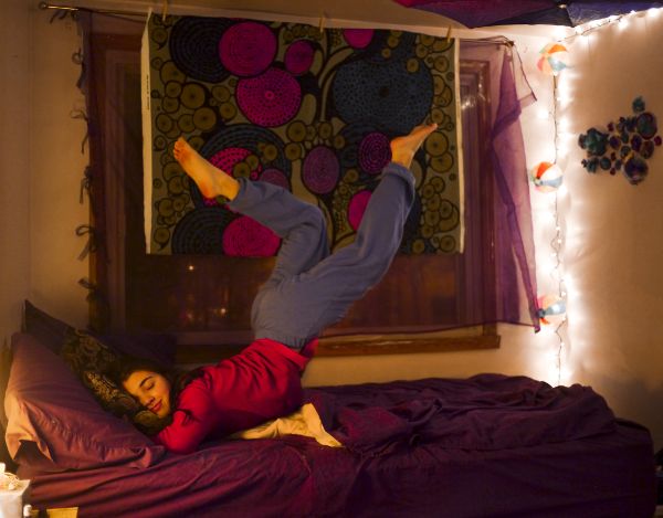 A woman sleeping in bed with her legs kicked up into the air.
