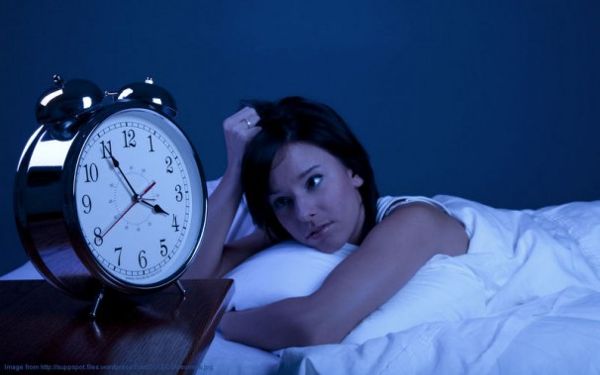 A woman is laying in bed at night staring at the clock.