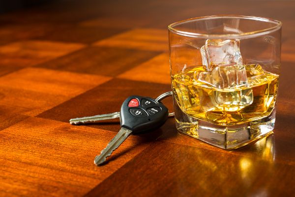Car keys next to a glass of whiskey on a table.